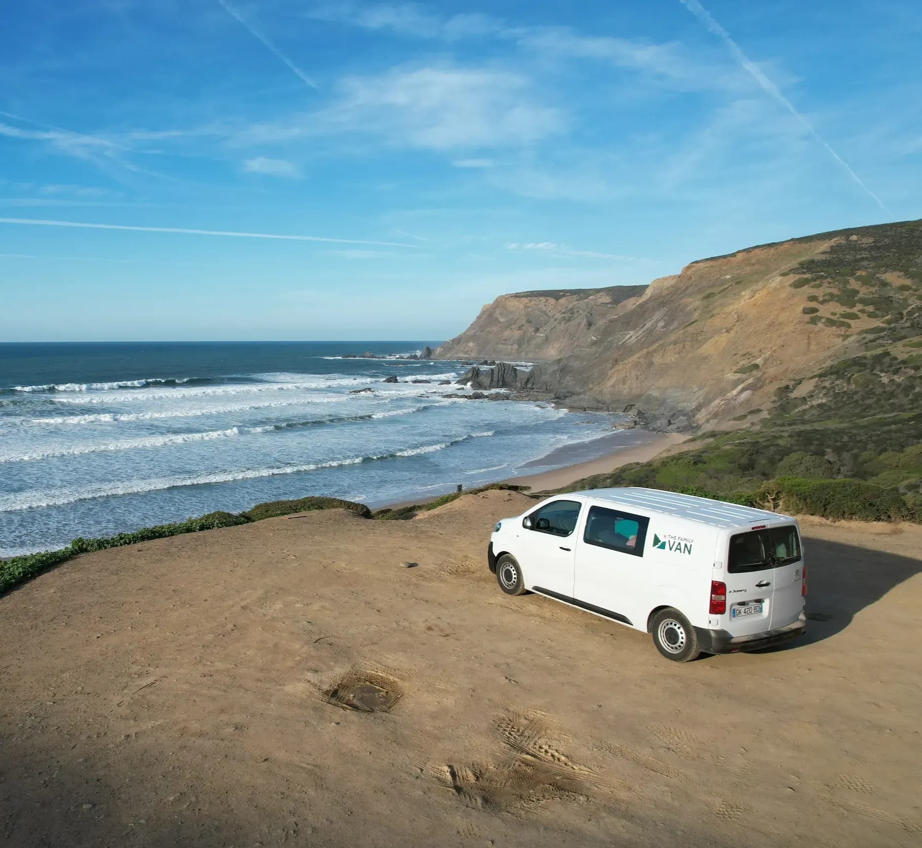 Campervan garé sur un promontoire de terre au-dessus d'une plage battue par de longs rouleaux