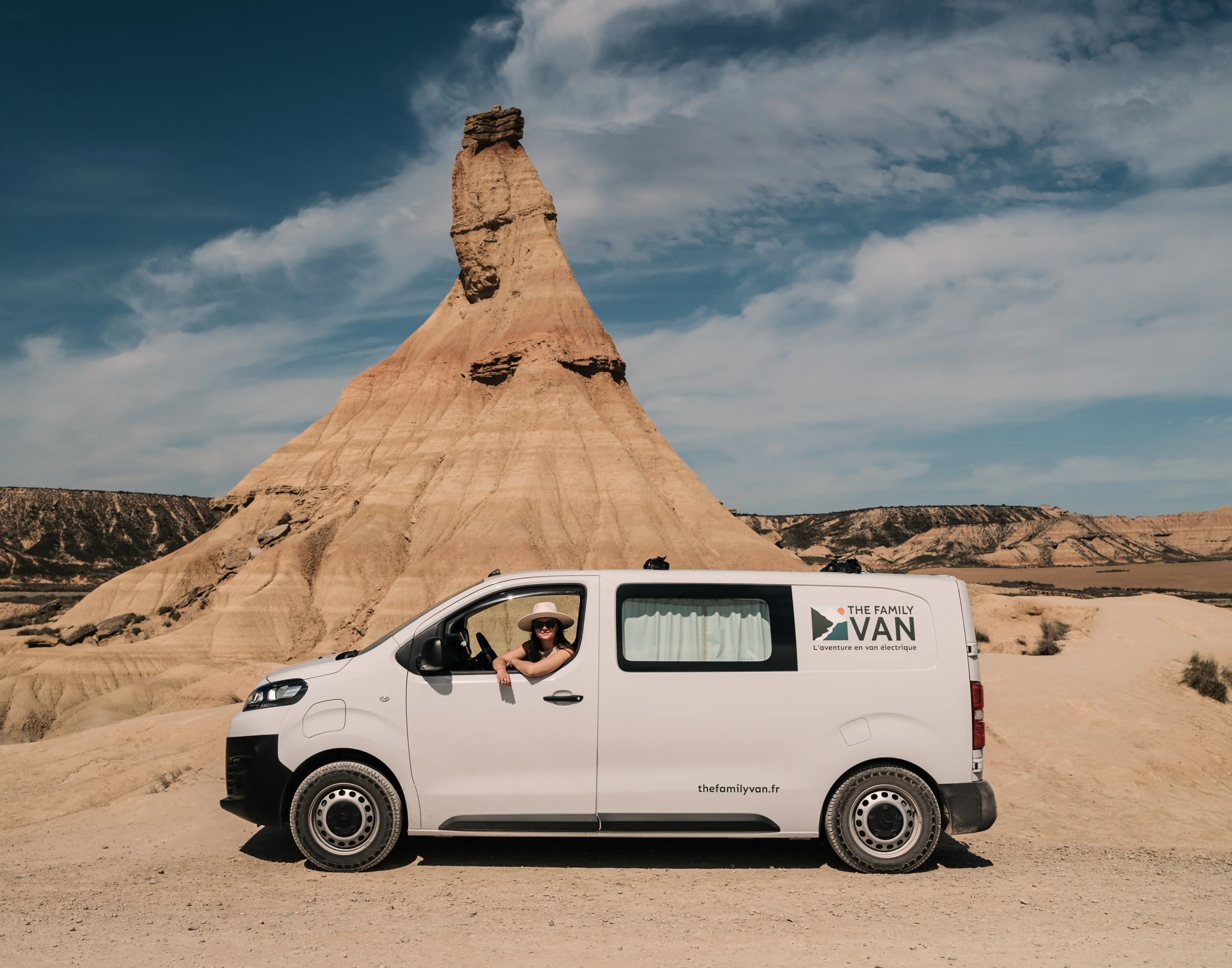 Campervan The Family Van arrêté devant la cheminée de fée du désert des Bardenas, cliente à la fenêtre