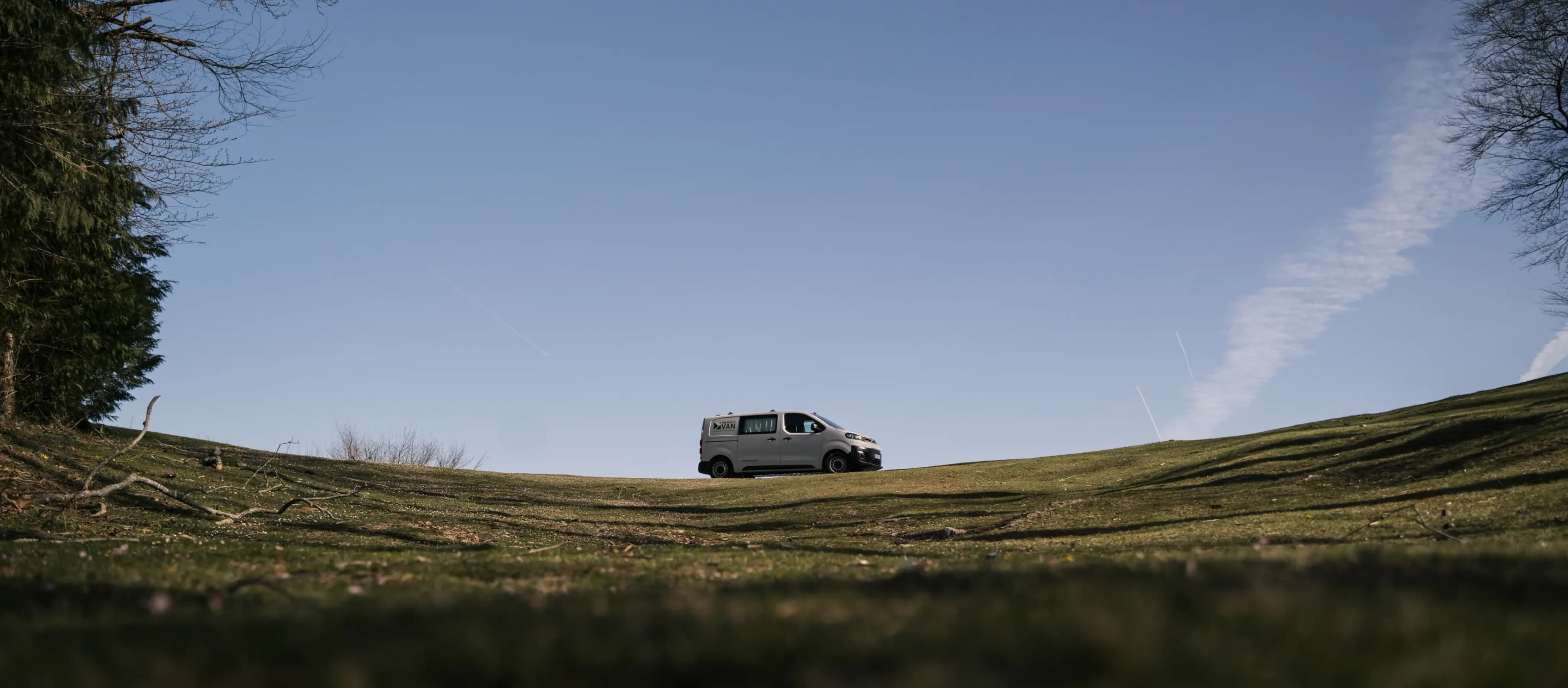 Campervan isolé sur une crête herbeuse sous un grand ciel bleu, photographié au ras du sol