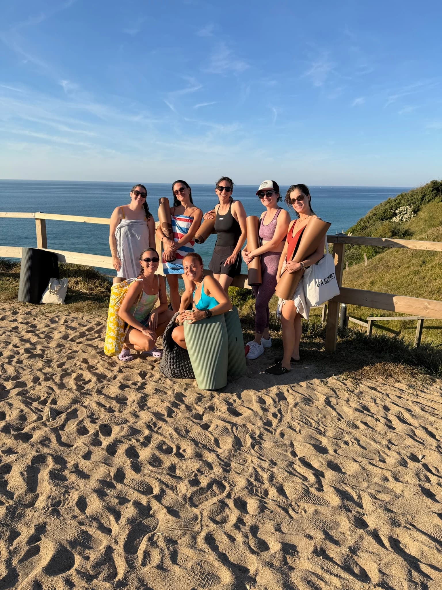 Groupe de femmes posant avec leurs tapis de yoga sur un chemin de sable au-dessus de l'océan