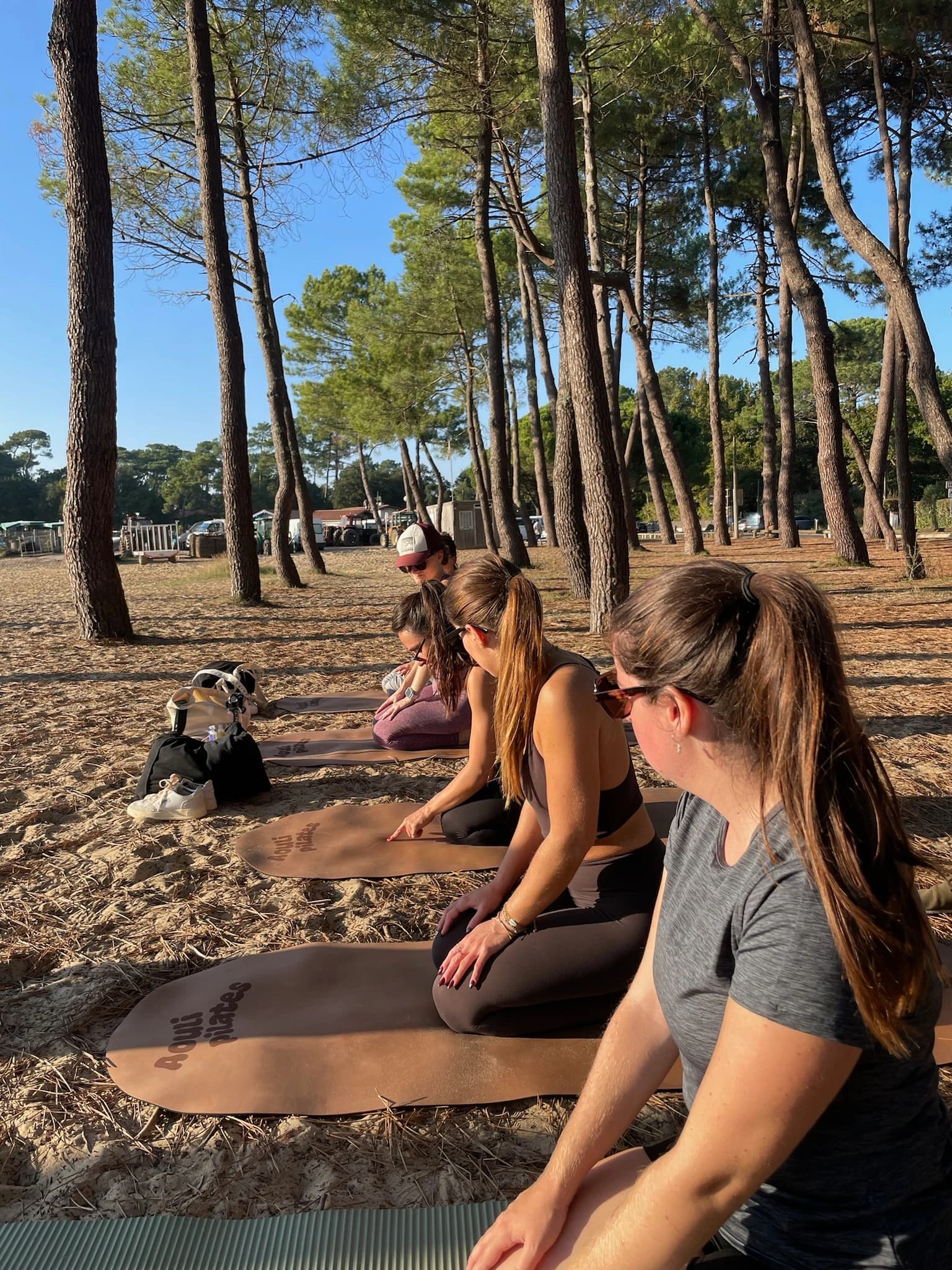 Femmes assises sur des tapis de pilates entre les pins, séance matinale sur le sable