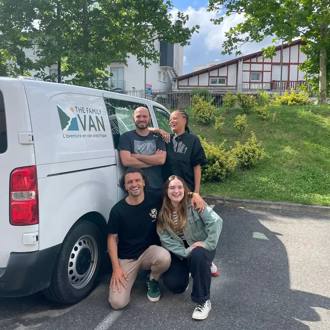 Quatre membres de l'équipe posent en riant devant un campervan floqué The Family Van