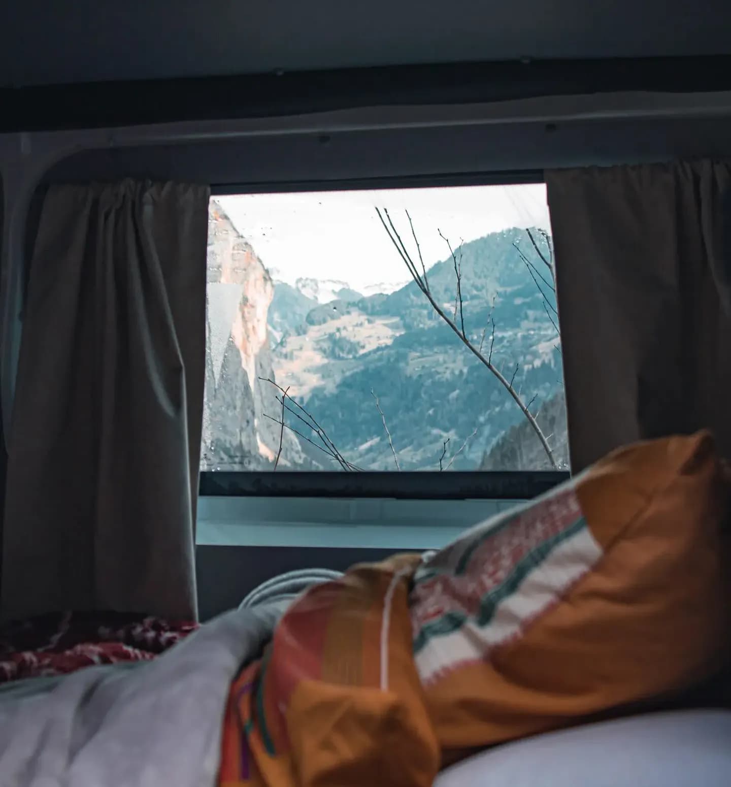 Depuis le lit du van, fenêtre ouverte sur une vallée de montagne enneigée, plaid coloré