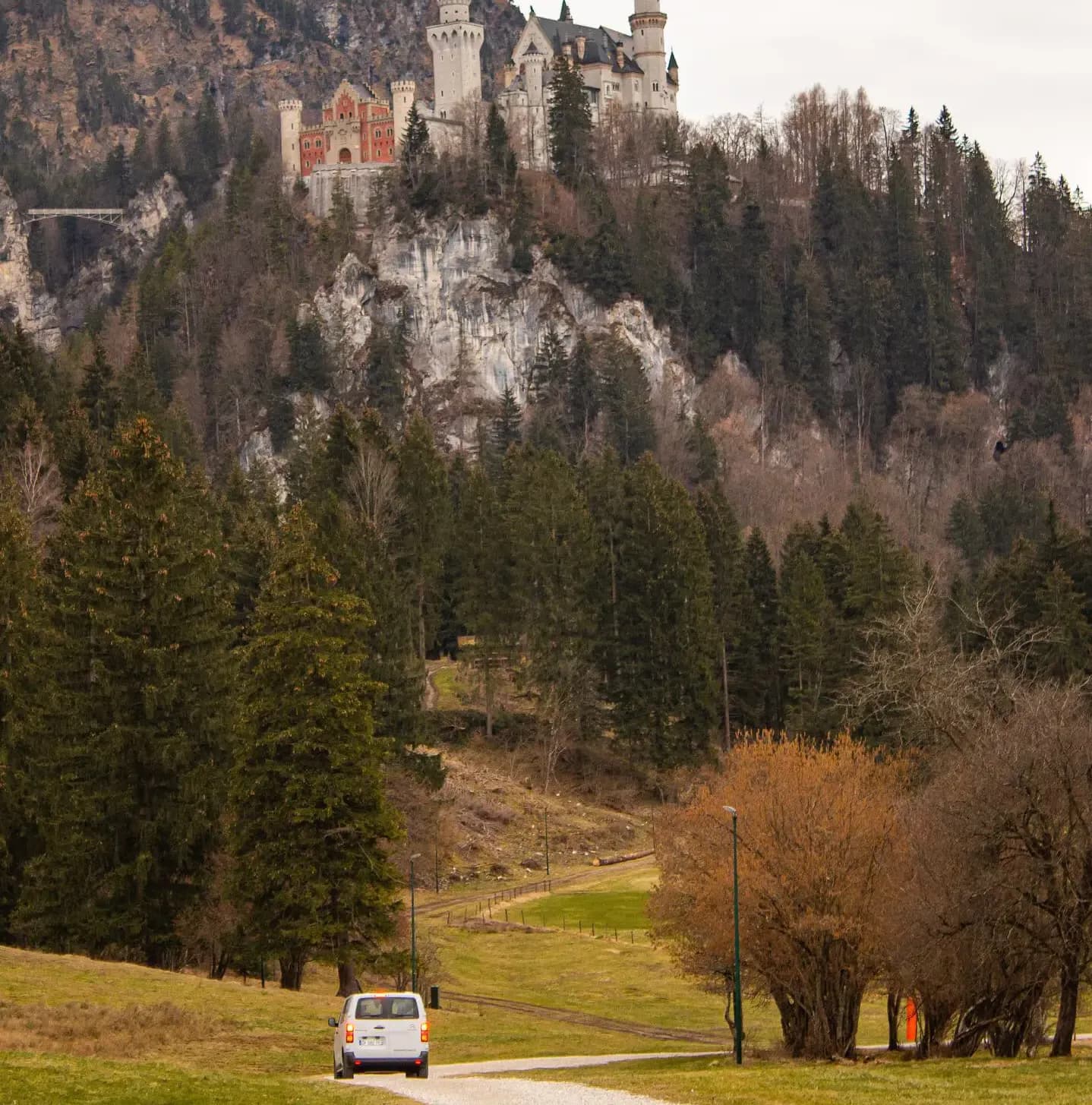 Van blanc sur une petite route de campagne, au pied d'une colline boisée dominée par un château