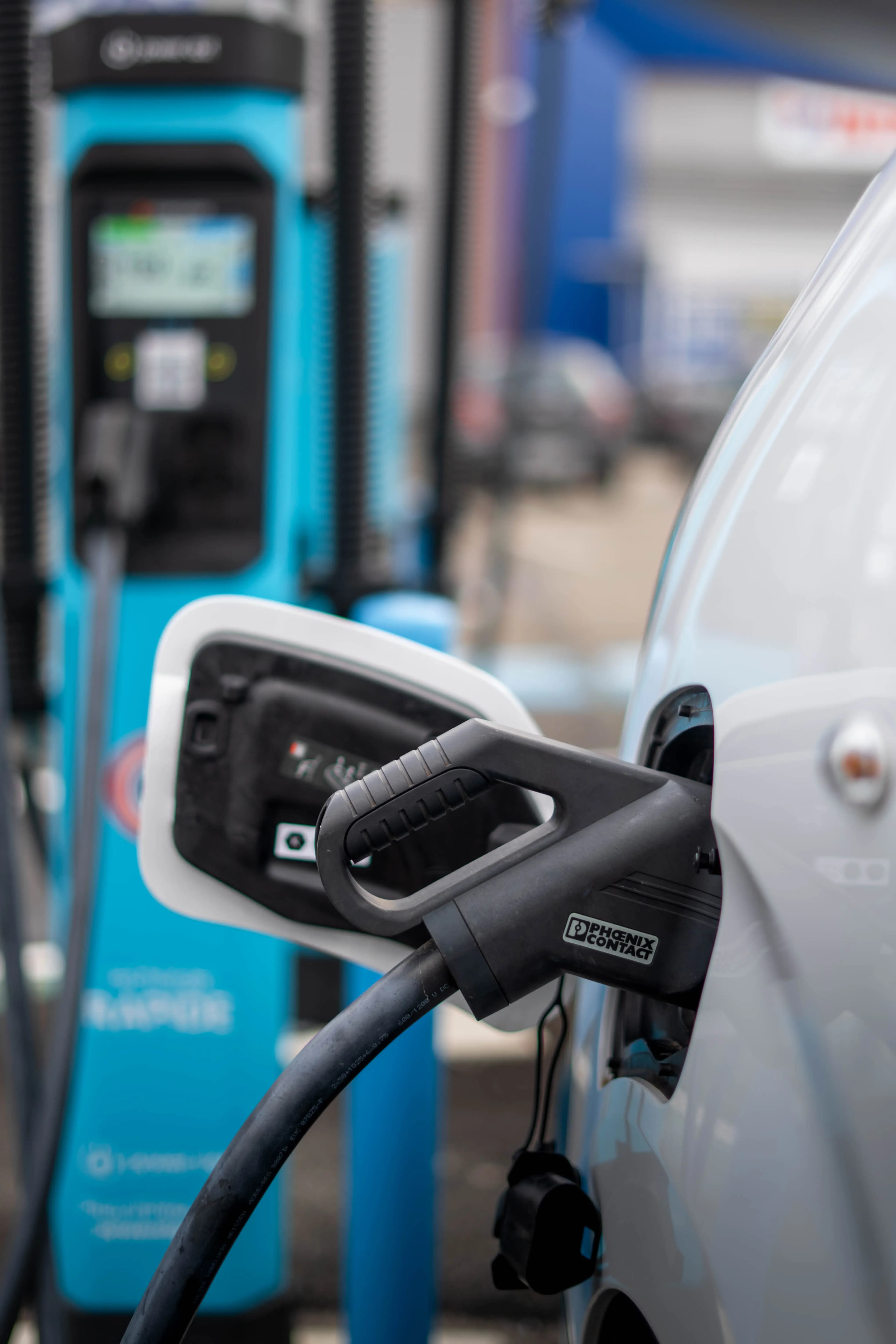 Câble branché sur la trappe de recharge d'un van électrique, borne de recharge bleue derrière