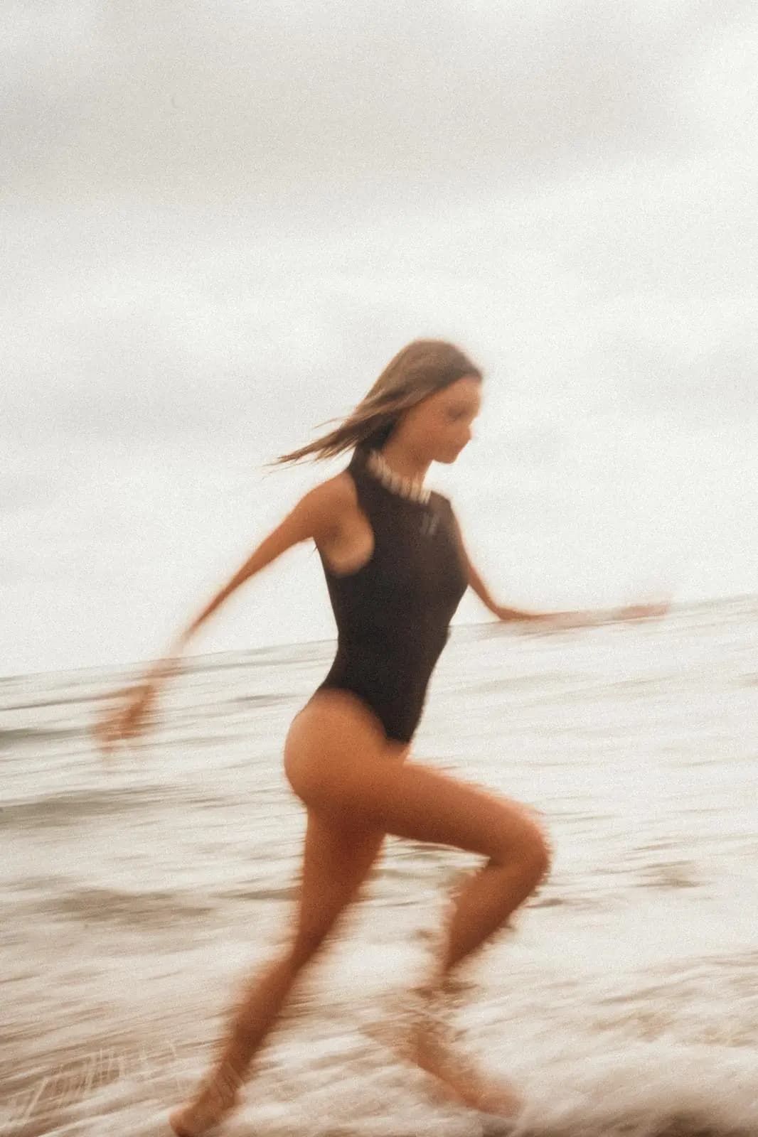 Une femme en maillot noir court dans l'écume, l'image saisie en léger flou de mouvement