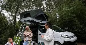 Tente de toit déployée sur un van aménagé, deux voyageuses préparent à manger à côté