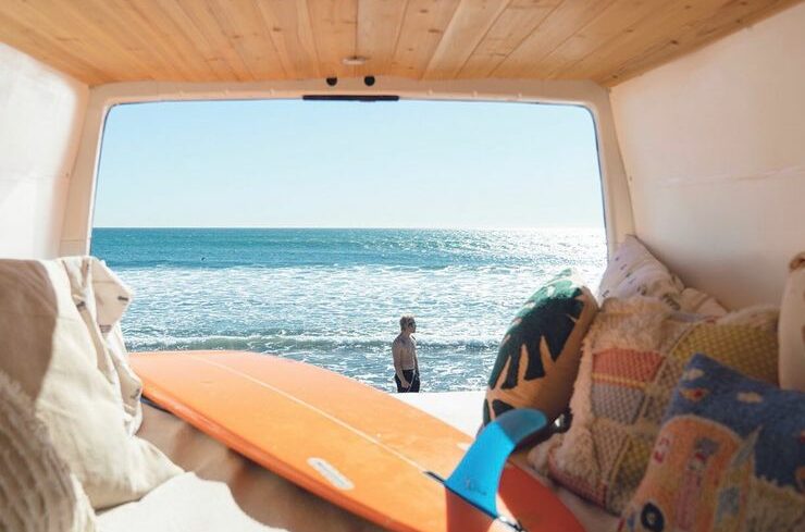 Photo d'un van aménagé électrique avec une planche de surf sur la plage